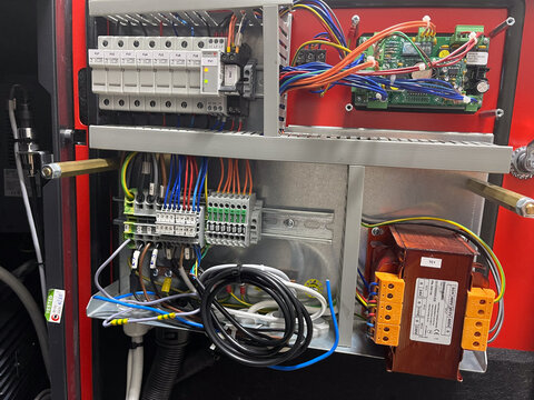 Industrial electrical control panel box with circuit breakers, transformer, and wiring harness. Open automated machinery switchboard background for engineering service and equipment repair website des