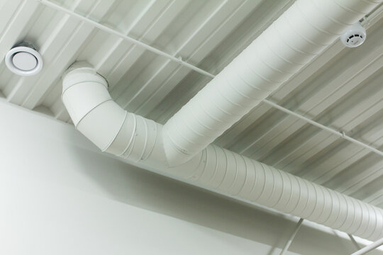 White spiral ventilation duct t-junction on ceiling for industrial hvac system website design. Air conditioning pipe background for climate control and engineering company mockups.