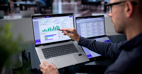 Obraz premium Young Man Uses Dual Touchscreen Laptops For Strategic Supplier Evaluation