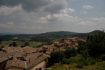 Obraz premium Terracotta rooftops of a historic Tuscan village overlooking rolling green countryside beneath dramatic clouds in Tuscany, Italy.