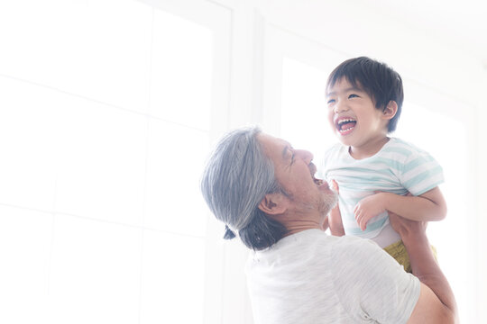逆光の中子どもを高い高いをして、抱っこして遊ぶグレイヘアの祖父 孫とのふれあい・育児や子育て、成長の明るいイメージ