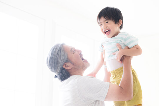 逆光の中子どもを高い高いをして、抱っこして遊ぶグレイヘアの祖父 孫とのふれあい・育児や子育て、成長の明るいイメージ