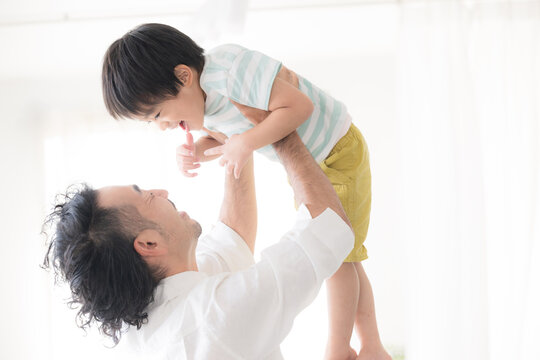 逆光の中子どもを高い高いをして、抱っこして遊ぶ父親 親子のふれあい・育児や子育て、成長の明るいイメージ