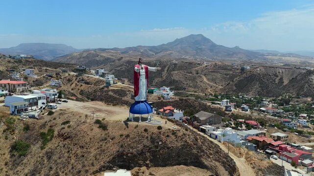 Close up aerial orbit around Christ of the Sacred Heart (Cristo del Sagrado Coraz&oacute;n) statue in Rosarito, Baja California, Mexico, surrounded by homes in residential area