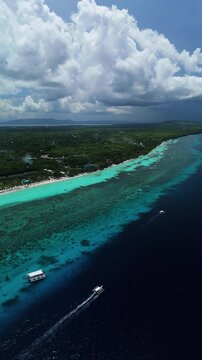 Vertical drone tracks a longboat and pans left to reveal Dumaluan Beach, reef flats, and blue coastal water in Panglao