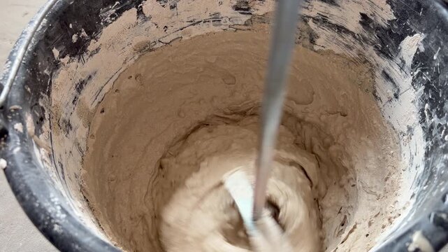 Close-up of a mechanical mixer blending beige plaster or mortar in a black bucket