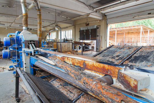 Blue industrial log debarker processing timber on rusty conveyor