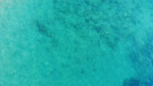 Aerial view of crystal clear turquoise sea revealing the natural underwater patterns of the shallow coastal waters on a sunny day.