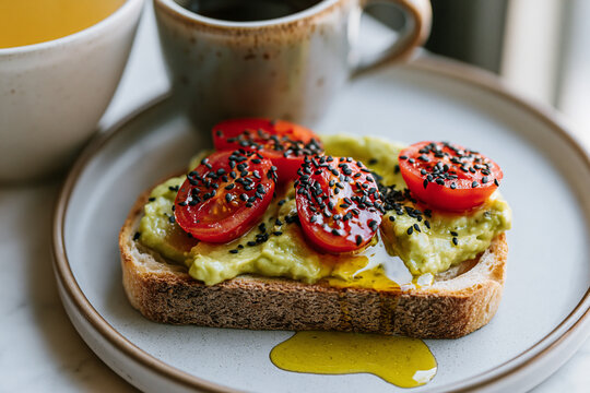 A slice of artisan bread topped with mashed avocado, ripe cherry tomatoes, a sprinkle of black sesame seeds and olive oil.