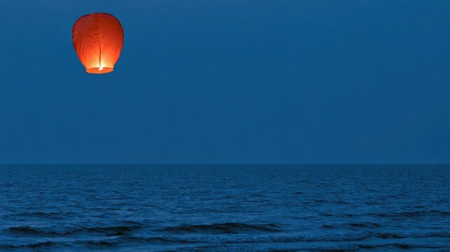 Glowing paper lantern drifts across dark sea under twilight sky