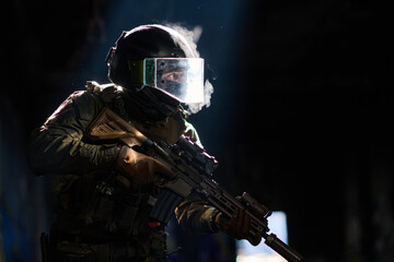Obraz premium Tactical Soldier in Ballistic Helmet and Face Shield Holding Assault Rifle in Low Light Smoke