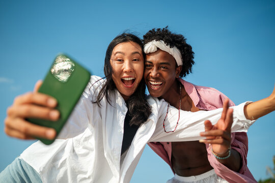Trendy digital creator couple taking selfie by the beach, sharing travel content for social media