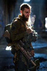 Obraz premium Bearded Soldier in Tactical Gear Holding Helmet and Rifle in Dim Industrial Building