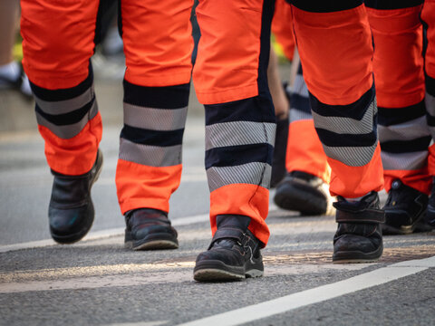 Close-up of emergency service personnel wearing high-visibility orange trousers with reflective bands and black safety boots while marching together