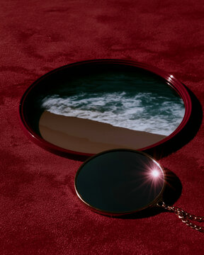Round black compact mirror showing ocean surf on red velvet. Perfect for surreal decor, luxury branding, and conceptual editorial use.
