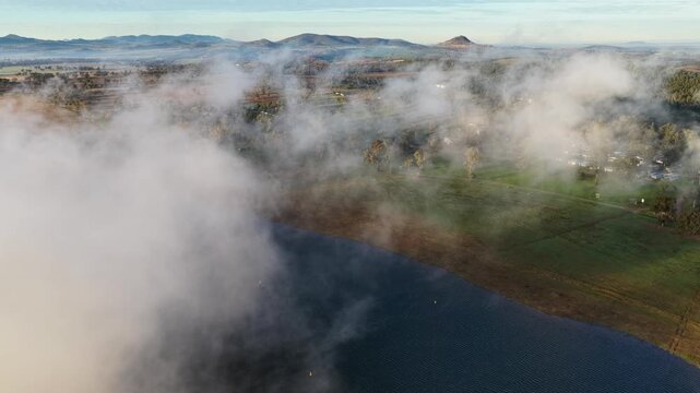 Aerial video of Lake Keepit Dam blanketed by morning fog in NSW, Australia. Low cloud drifts across the reservoir and surrounding landscape
