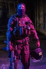 Obraz premium Armed Tactical Soldier In Night Operation Wearing Ballistic Vest Holding Helmet And Rifle