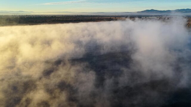Aerial video of Lake Keepit Dam blanketed by morning fog in NSW, Australia. Low cloud drifts across the reservoir and surrounding landscape
