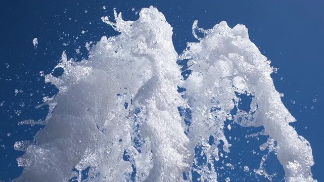 Close-up of white fountain water jets against clear blue sky. Foamy splashes create refreshing abstract texture symbolizing freshness, summer, purity and movement