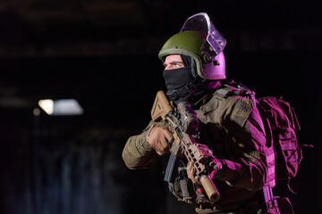 Obraz premium Tactical Soldier In Helmet And Balaclava Holding Assault Rifle During Night Urban Operation