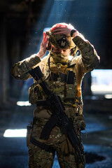 Obraz premium Soldier In Tactical Camouflage Adjusting Helmet With Rifle In Dim Urban Interior Light