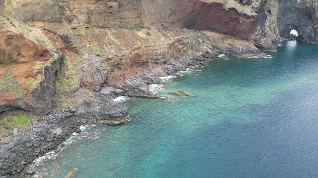 Drone aerial slow push forward shot of volcanic coastline and natural rock arch in Madeira