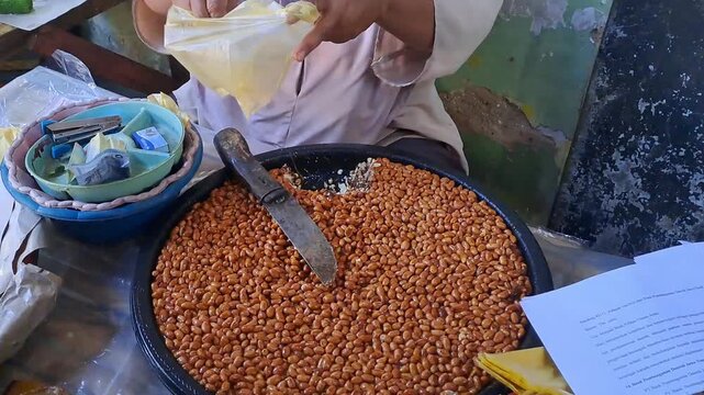 Indonesian vendor selling traditional Ting peanut candy. Roasted peanuts coated with palm sugar served on large tray. Authentic jajanan tradisional and sweet snack from local market culture.