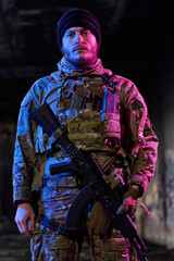 Obraz premium Armed Soldier In Camouflage Tactical Gear Holding Rifle Under Neon Urban Lighting At Night