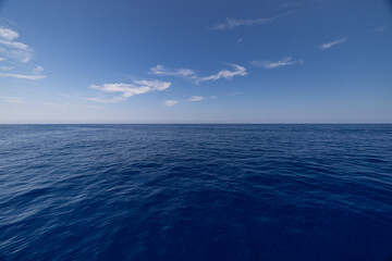 Obraz premium Peaceful perfect deep blue sea waves background under wide open sky soft clouds bright horizon. Beautiful minimal ocean nature seascape landscape. Serene tranquil natural water view wallpaper art