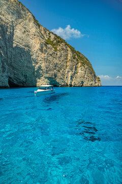 Breathtaking white cliffs above crystal turquoise bay with boat clear shallow water summer Greece. Beautiful coastal nature seascape landscape. Scenic Mediterranean travel escape, transparent lagoon