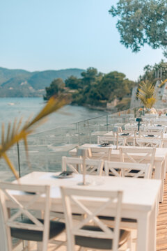 Charming resort terrace dining beside ocean view under palm frame stylish table Mediterranean coast summer. Elegant coastal lifestyle hospitality scene. Romantic seaside restaurant holiday