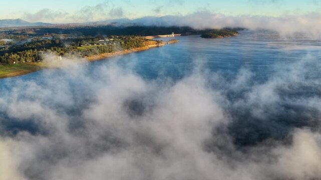 Aerial video of Lake Keepit Dam blanketed by morning fog in NSW, Australia. Low cloud drifts across the reservoir and surrounding landscape
