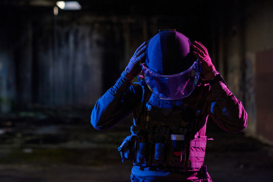 Tactical Officer in Riot Helmet and Body Armor Preparing in Abandoned Urban Warehouse With Neon Light