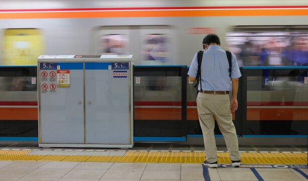 Back view of a Japanese commuter waiting on a subway platform with a motion blurred train passing by, Tokyo, Japan.
