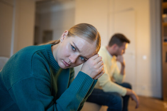 Stressed married couple sitting on couch distancing from each other after emotional family argument, frustrated woman in offence to partner, emotional crisis, coldness and mistrust in relationships.
