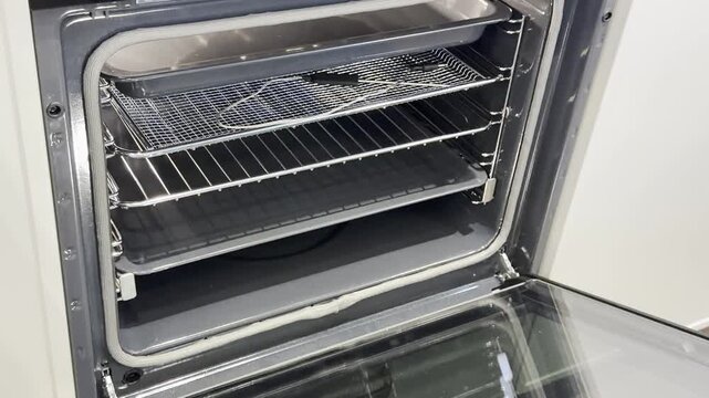 Open oven with metal racks and glass door, clean kitchen appliance interior seen from the front