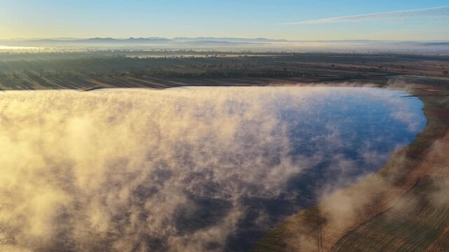 Aerial video of Lake Keepit Dam blanketed by morning fog in NSW, Australia. Low cloud drifts across the reservoir and surrounding landscape
