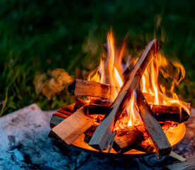 Campfire with wood stacked in a teepee shape burning on green grass at a campsite at dusk © AK Photo