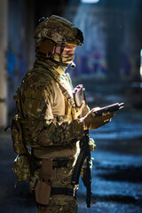 Obraz premium Tactical Soldier in Camouflage Gear With Rifle and Tablet Inside Dim Urban Building Light