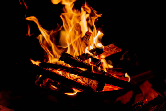 Vivid orange campfire flames rising from burning logs against a dark background at night