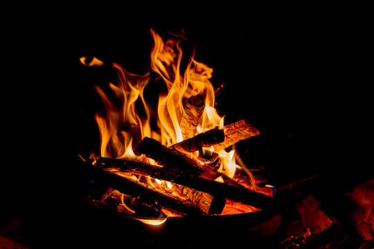 Dancing campfire flames over glowing embers and burning wood on a dark night background