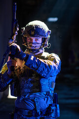 Obraz premium Armed Soldier In Tactical Gear Aiming Rifle Under Dramatic Blue Lighting In Urban Environment