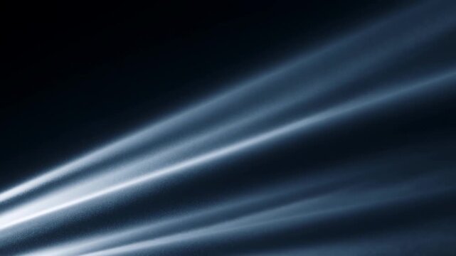 Slow motion tracking pan tilt shot of light beams sweeping across dark textured surface in studio setting