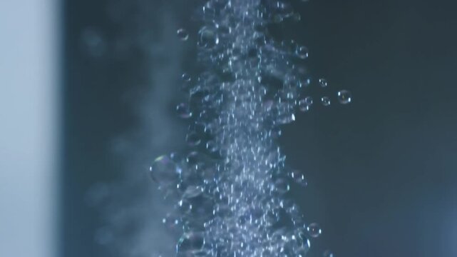 Slow motion vertical tracking closeup of bubbles rising in water column inside glass tank in studio lab setting