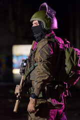 Fototapeta premium Armed Tactical Soldier In Helmet And Gear Holding Rifle With Night Urban Background