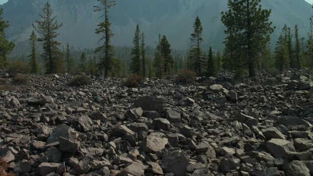 Rocky volcanic terrain with scattered conifer trees and mountain range in the background, Lassen Volcanic National Park, California, USA. Zoom out reveal shot