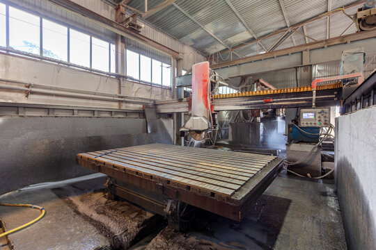 Industrial bridge saw cutting machine with a massive metal processing table in a stone factory workshop