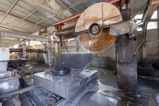 Large industrial circular saw machine with diamond blade disc processing natural granite block in a stone cutting factory in Karelia