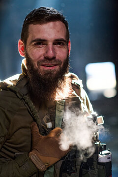 Bearded Soldier in Tactical Gear Smiling While Cold Breath Is Visible in Dim Light