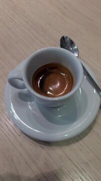 Freshly brewed italian espresso with a rich crema served in a classic white ceramic cup on a saucer with a spoon, sitting on a wooden table in a cafe, perfect for a morning energy boost